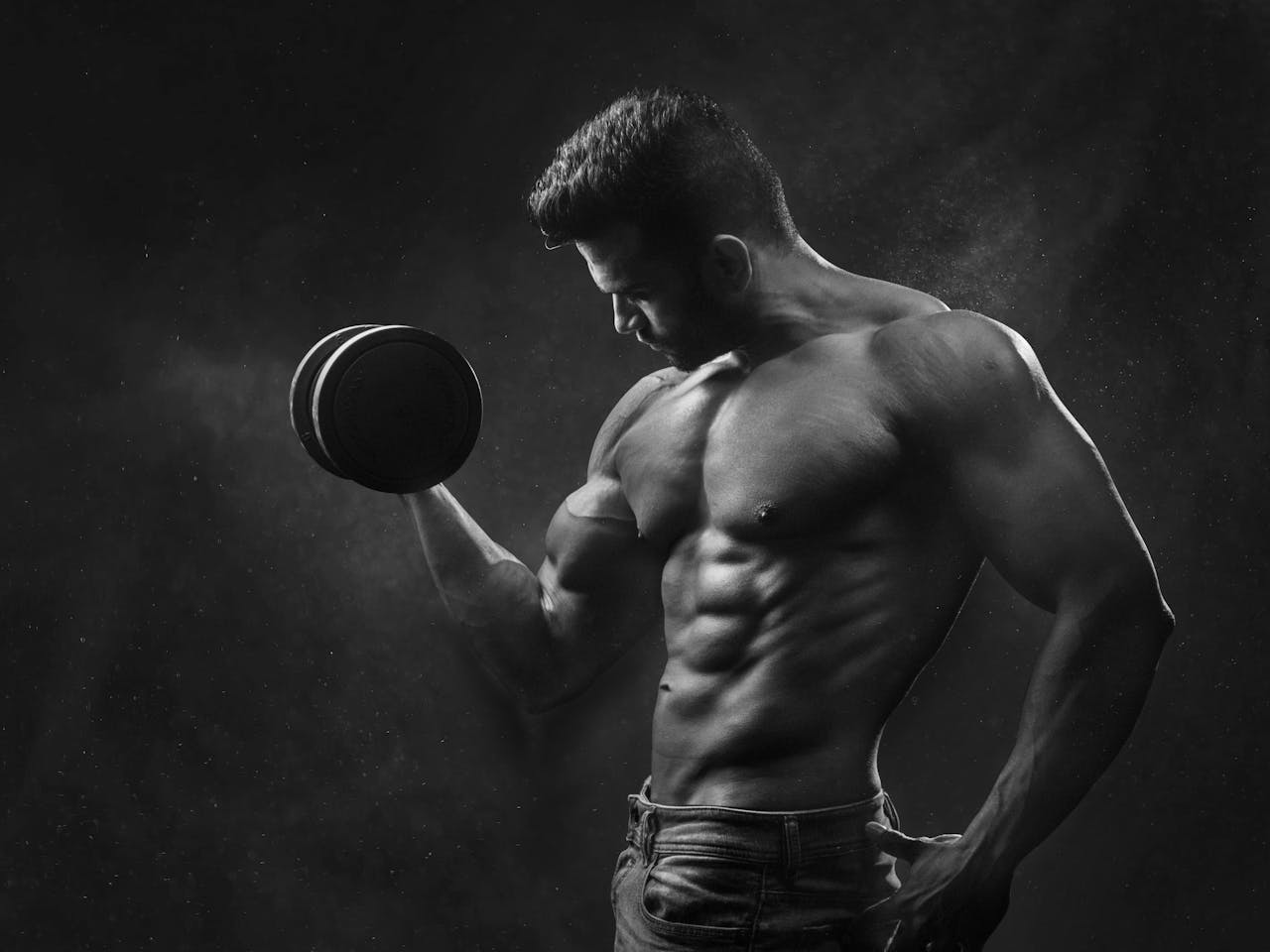 Powerful black and white portrait of a shirtless bodybuilder lifting dumbbells in the gym.