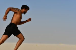 A muscular man sprinting shirtless through a desert, showcasing strength and determination.